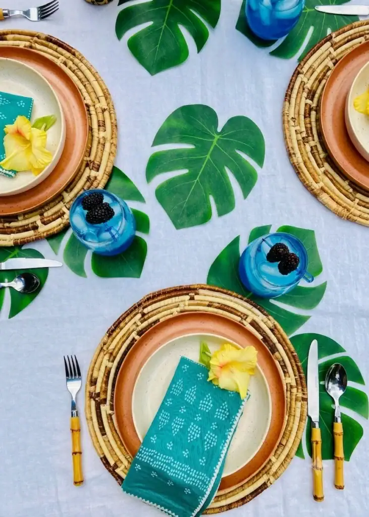 Aladdin's Blue Calypso Cooler mocktail in stemless glasses with vivid blue Calypso lemonade, ice, and fresh blackberry garnish on blue cocktail picks, styled on a tropical table with monstera leaves and woven placemats for an Enchanted Tiki Room Disney brunch.