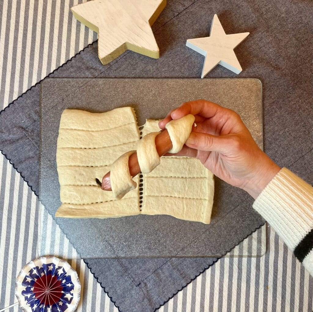 Golden breadstick-wrapped hot dog on a bamboo skewer with a yellow cheese star on top, styled for a 4th of July Captain America cookout.