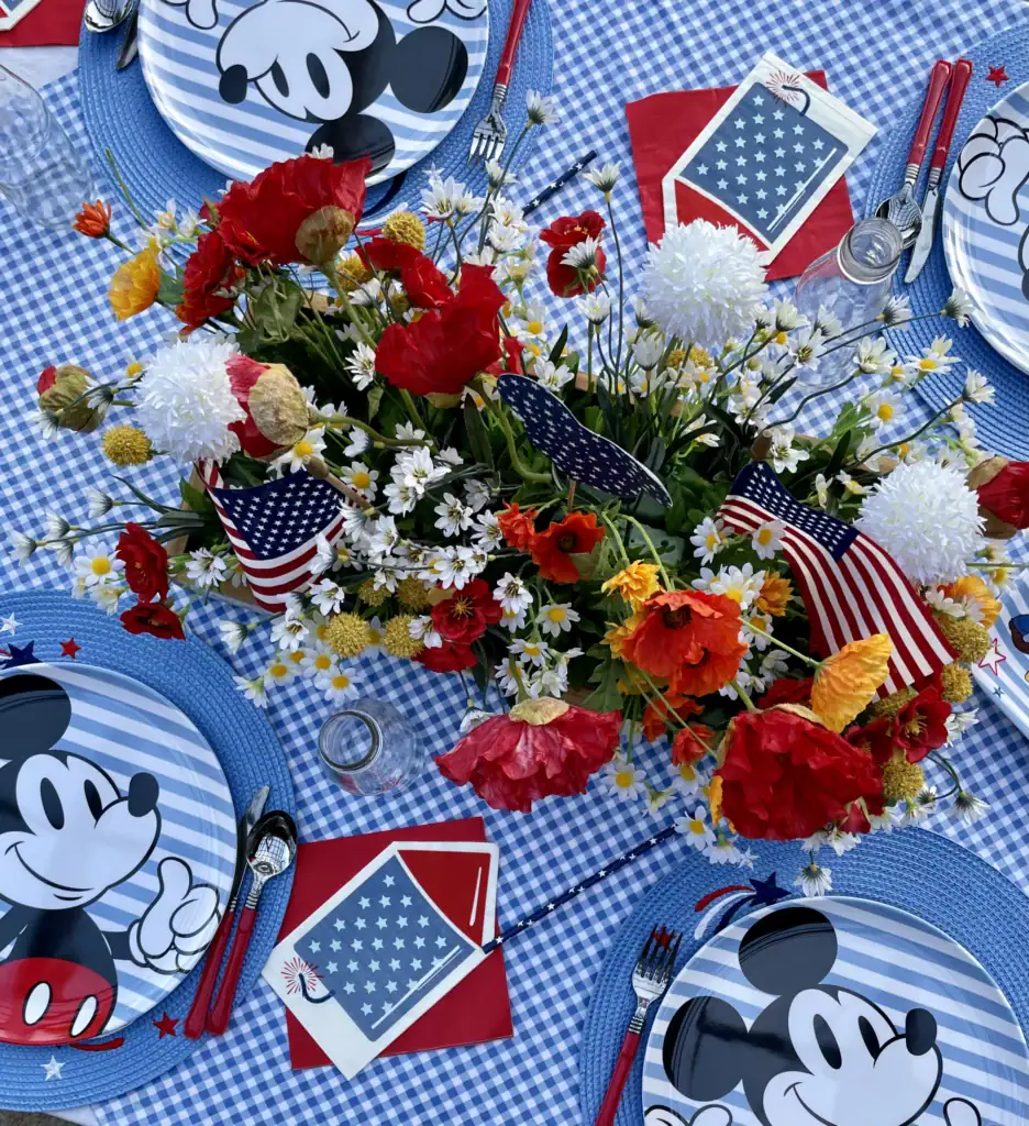 Patriotic Disney tablescape with blue gingham runner, retro Mickey plates, and wildflower centerpiece for the 4th of July